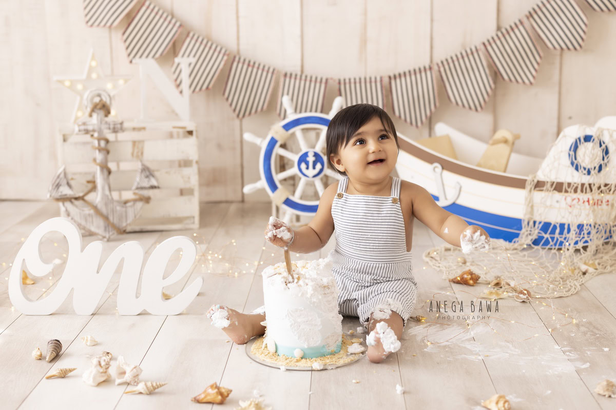 1 year old boy playing with Cake Smash, toy spaceship, beige backdrop, first birthday photography in Delhi, Gurgaon. Captured by Anega Bawa family photographer Gurgaon (Delhi NCR)