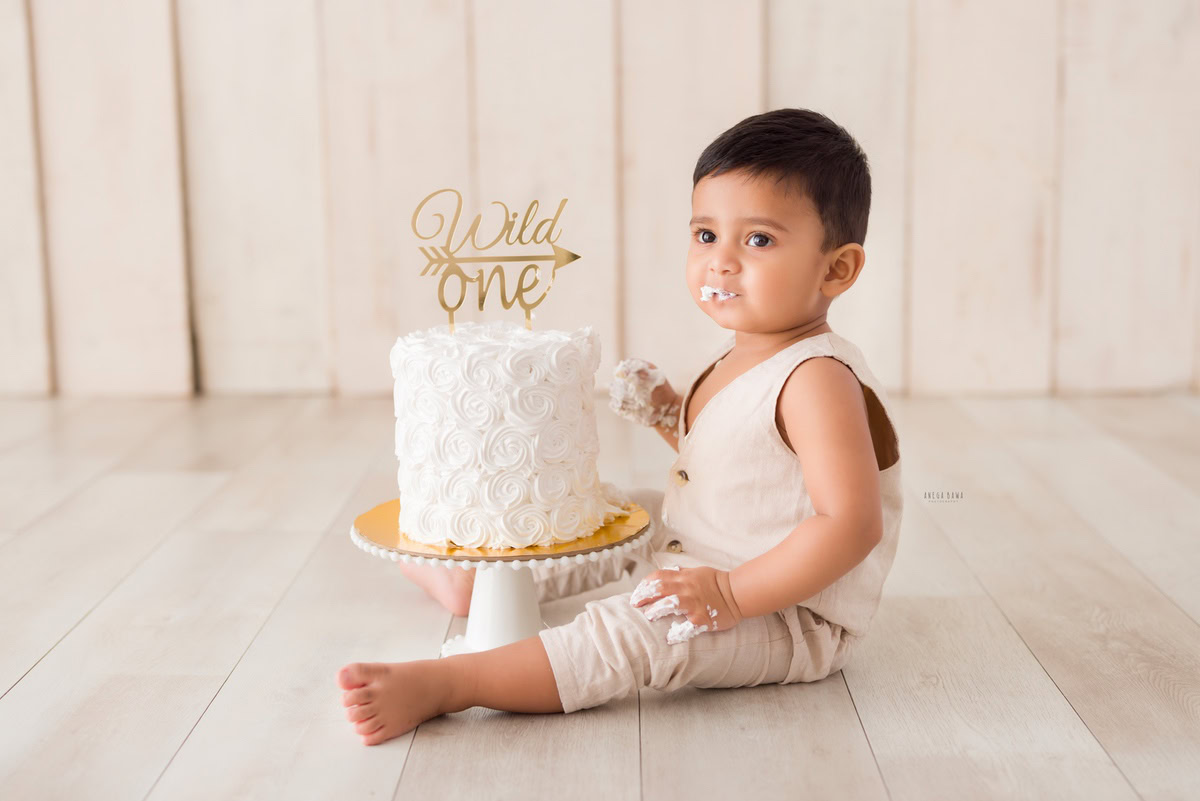 1year old boy posing with a cake smash setup against a beige backdrop, captured by Anega Bawa during a Cake Smash photoshoot in Delhi, Gurgaon