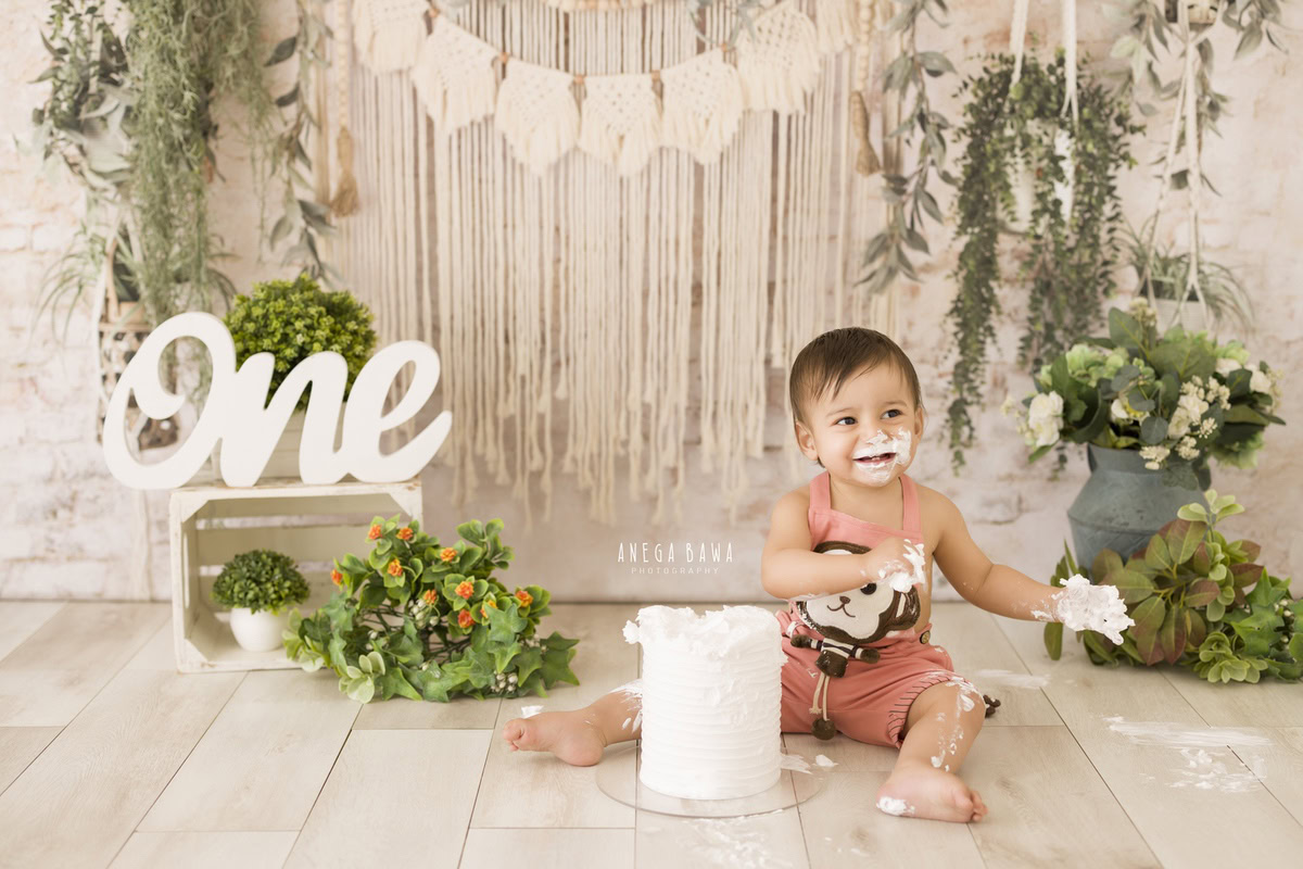 1 year old boy sitting on floor with Cake Smash, white pots, beige net backdrop, first birthday photo shoot in Delhi, Gurgaon. Captured by Anega Bawa family photographer Gurgaon (Delhi NCR)