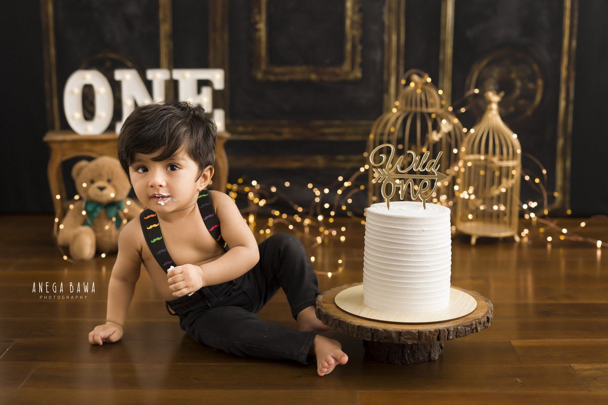 1year old boy sitting with a cake smash setup featuring golden castles and fairy lights against a brown backdrop, captured by Anega Bawa during a Cake Smash photoshoot in Delhi, Gurgaon