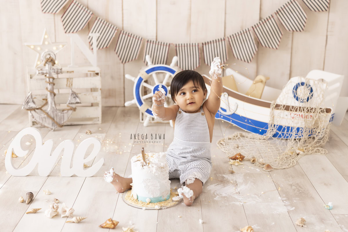 1year old boy with a toy spaceship and cake smash setup against a beige backdrop, captured by Anega Bawa during a Cake Smash photoshoot in Delhi, Gurgaon