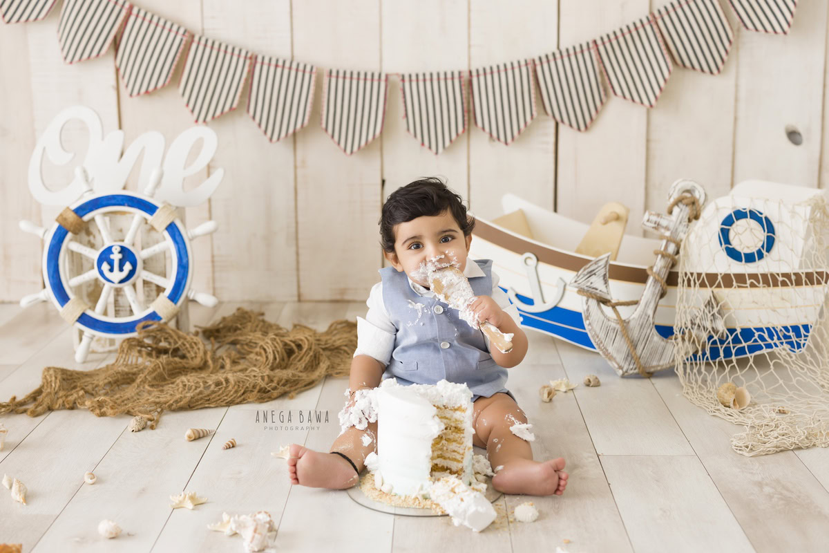 1 year old boy with a toy spaceship, beige backdrop, and brown rug. Captured during a fun first birthday photo shoot in Delhi Gurgaon by the renowned family photographer Anega Bawa.