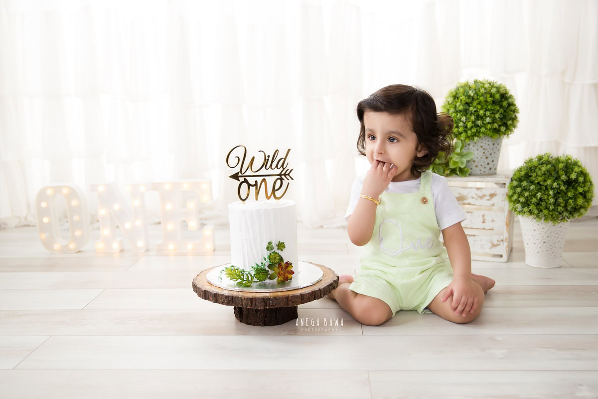 1 year old boy with a cake smash setup, featuring a white backdrop and white pots. Celebrating his first birthday. Cake Smash photo shoot in Delhi, Gurgaon by Anega Bawa Family Photographer Gurgaon (Delhi NCR).