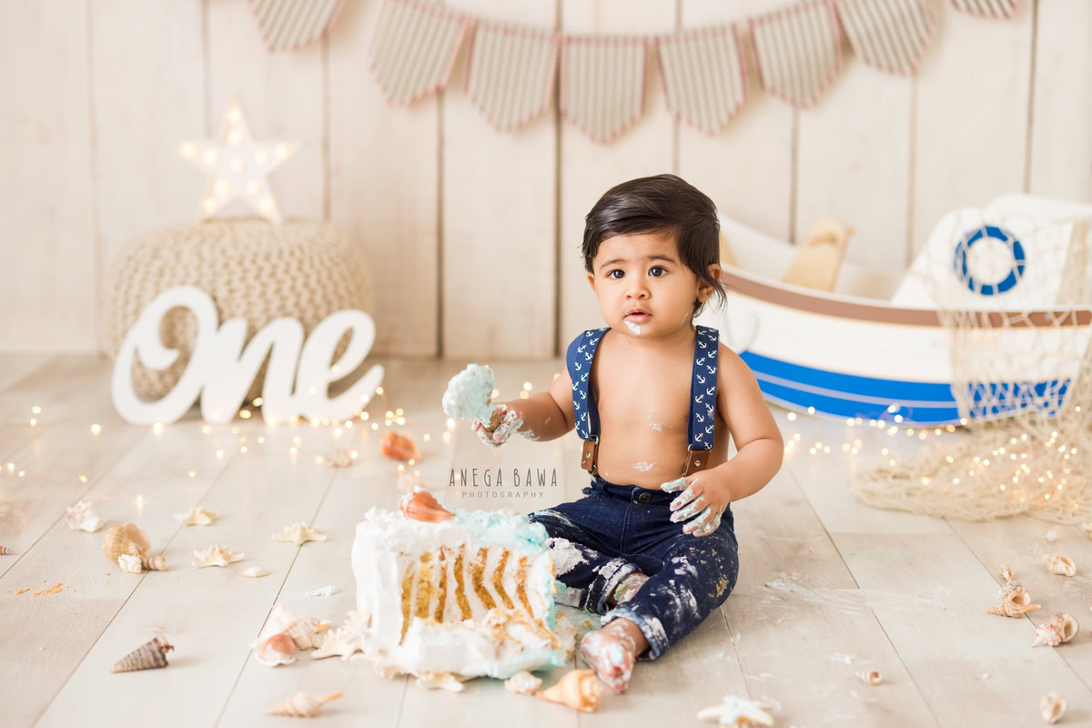 1year old boy with a cake smash setup and a toy spaceship against a beige backdrop, captured by Anega Bawa during a Cake Smash photoshoot in Delhi, Gurgaon