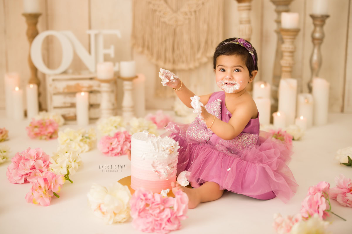 1 year old girl with beige backdrop, elegant candle stand, ivory and pink flowers on floor, first birthday photography in Delhi, Gurgaon. Captured by Anega Bawa family photographer Gurgaon (Delhi NCR)