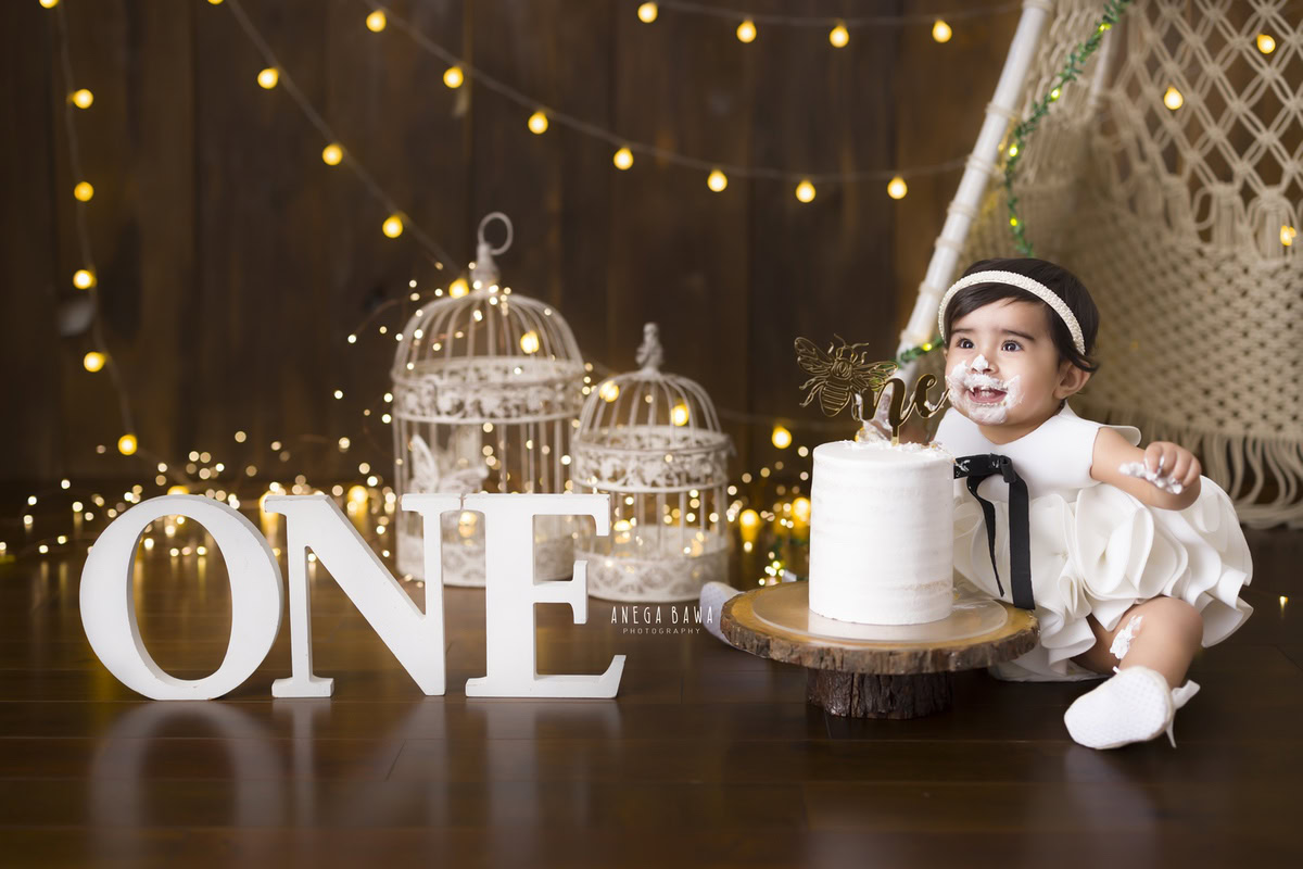 1year old girl with a cake smash setup featuring castles and fairy lights against a brown backdrop, captured by Anega Bawa during a Cake Smash photoshoot in Delhi, Gurgaon