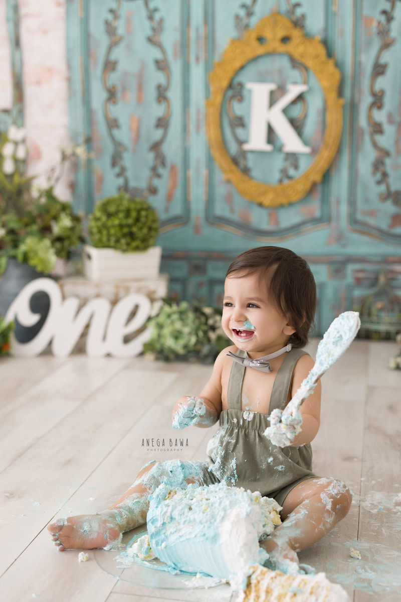 1 year old girl with cake smash, green door backdrop, and alphabet frame on the wall. Captured during a charming first birthday photo shoot in Delhi Gurgaon by the well-known family photographer Anega Bawa.