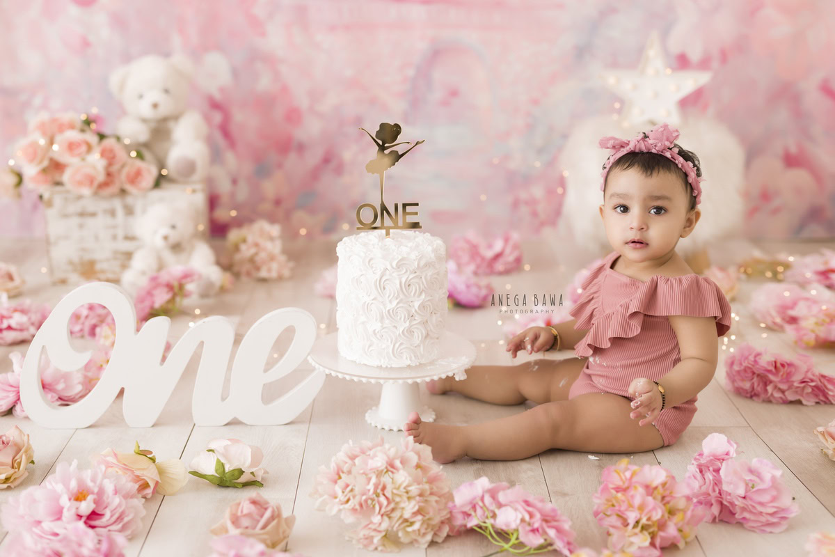 1year old girl with a cake smash setup against a pink backdrop featuring teddy bears, captured by Anega Bawa during a Cake Smash photoshoot in Delhi, Gurgaon
