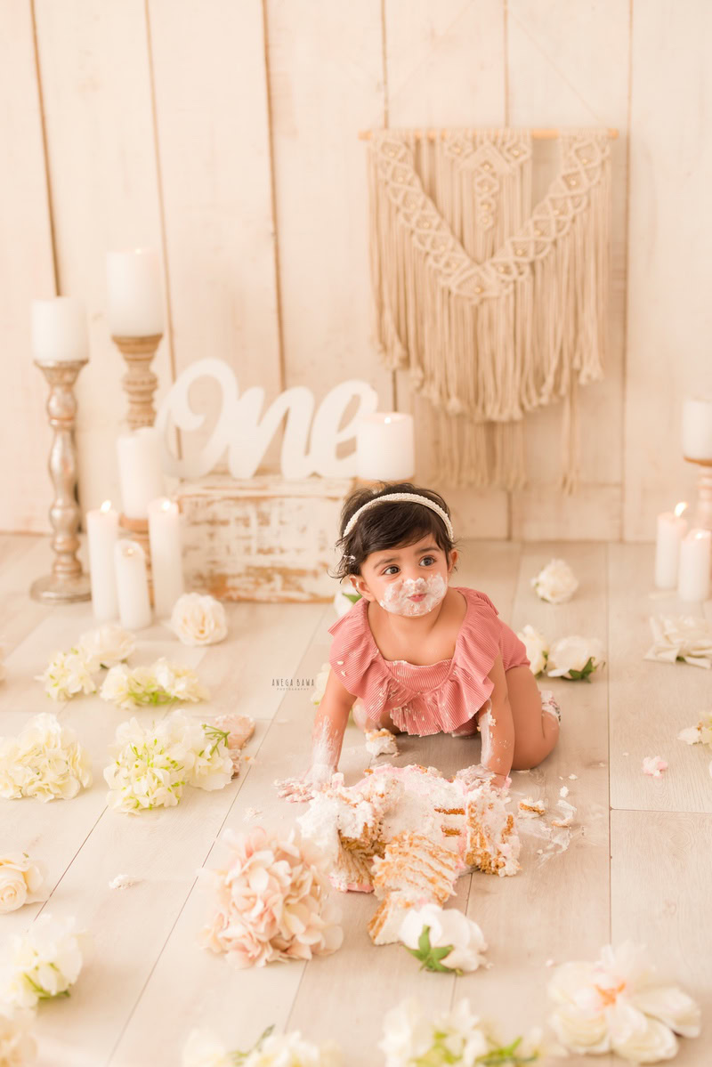 1year old girl crawling with cake on her face and a candle stand, against a beige backdrop, captured by Anega Bawa during a Cake Smash photoshoot in Delhi, Gurgaon