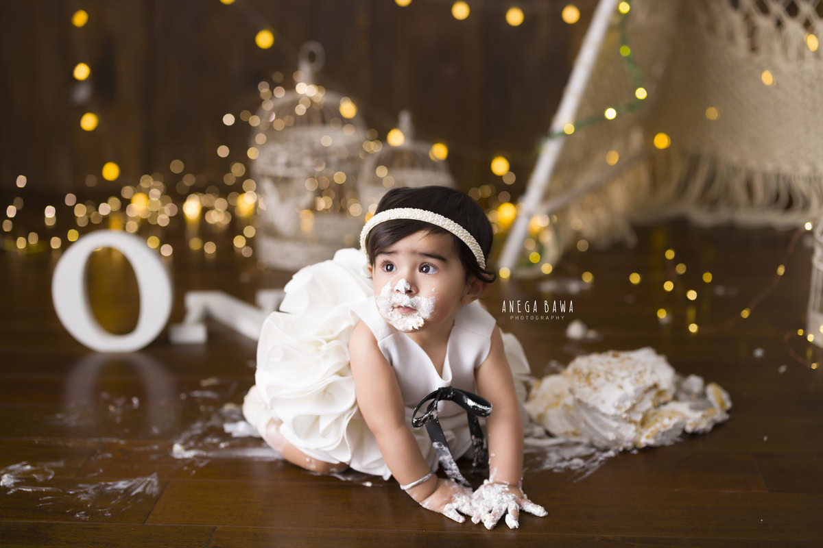 1 year old girl crawling on the floor with Cake Smash, surrounded by sparkling fairy lights and a warm brown backdrop, first birthday photography in Delhi, Gurgaon. Captured by Anega Bawa family photographer Gurgaon (Delhi NCR)