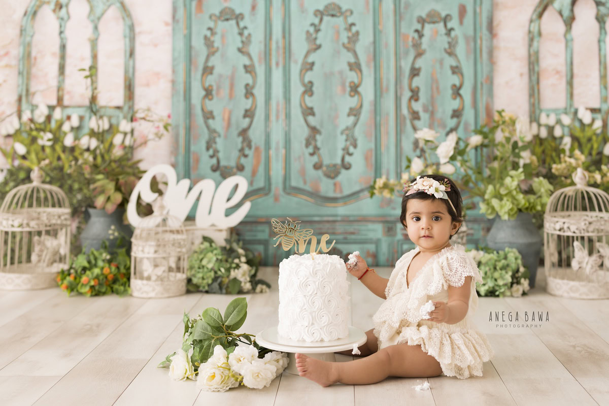 1year old girl with a cake smash setup and castles against a green door backdrop, wearing a cute tiara band, captured by Anega Bawa during a Cake Smash photoshoot in Delhi, Gurgaon
