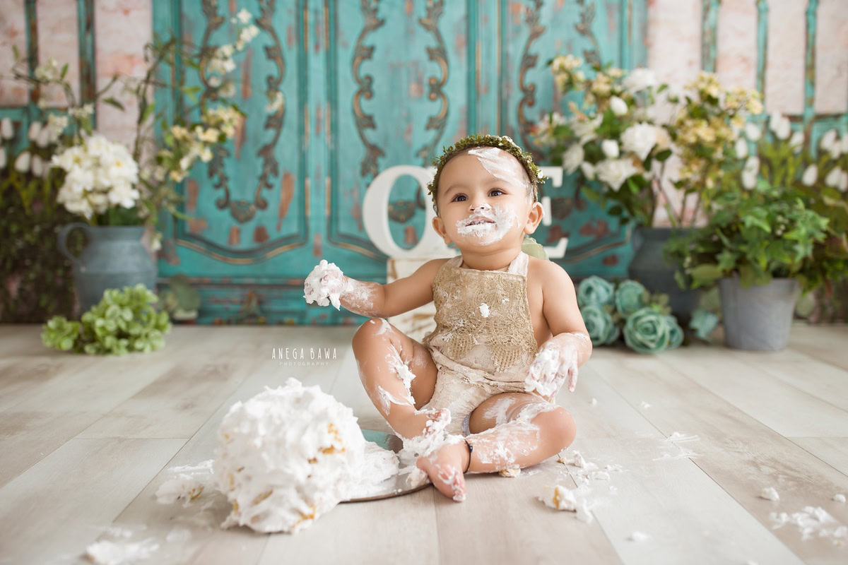 1 year old girl playing with a cake smash setup, featuring a green door backdrop. Celebrating her first birthday. Cake Smash photo shoot in Delhi, Gurgaon by Anega Bawa Family Photographer Gurgaon (Delhi NCR).