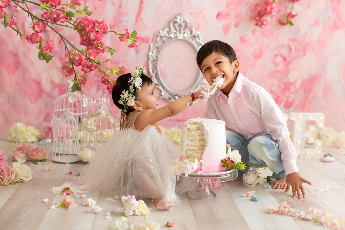 1 year old girl sibling with a castle, pink backdrop, and flowers on the floor. Captured during a charming first birthday photo shoot in Delhi Gurgaon by the renowned family photographer Anega Bawa.