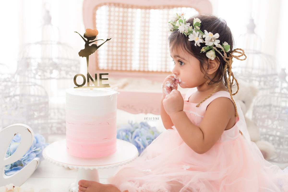 1year old girl wearing a tiara band with a cake smash setup featuring white castles against a white backdrop, captured by Anega Bawa during a Cake Smash photoshoot in Delhi, Gurgaon