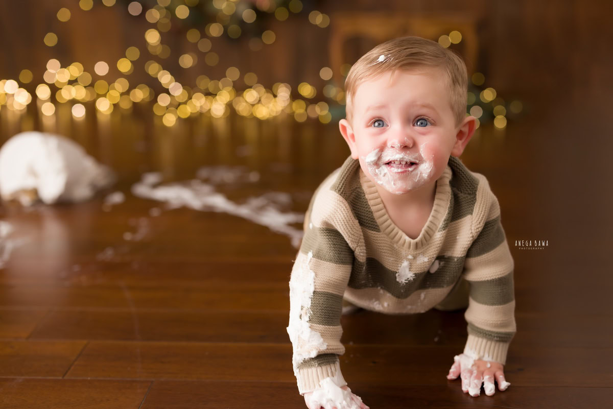 1year old boy with cake on his face and a cake smash setup against a brown backdrop with fairy lights, captured by Anega Bawa during a Cake Smash photoshoot in Delhi, Gurgaon