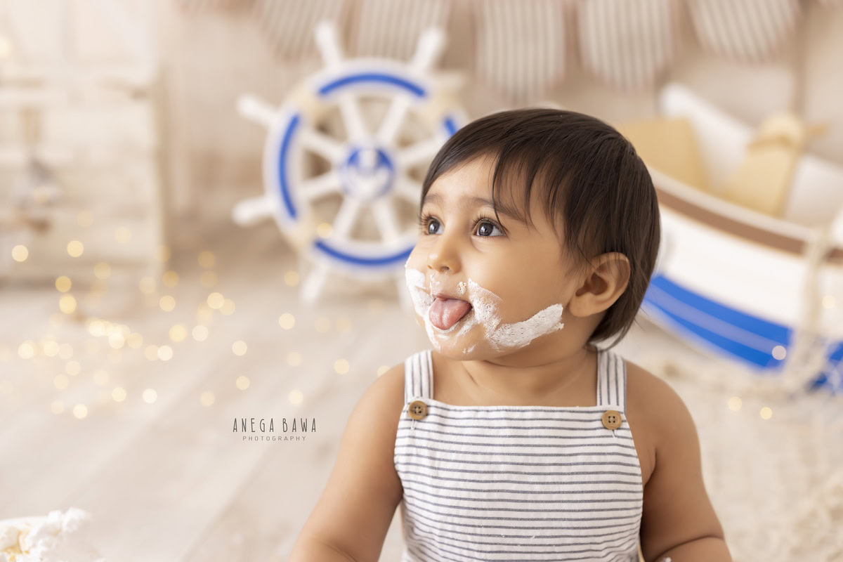 Boy with Cake Smash on face, sparkling fairy lights, toy spaceship, and a beige backdrop, first birthday photoshoot in Delhi, Gurgaon. Captured by Anega Bawa family photographer Gurgaon (Delhi NCR)