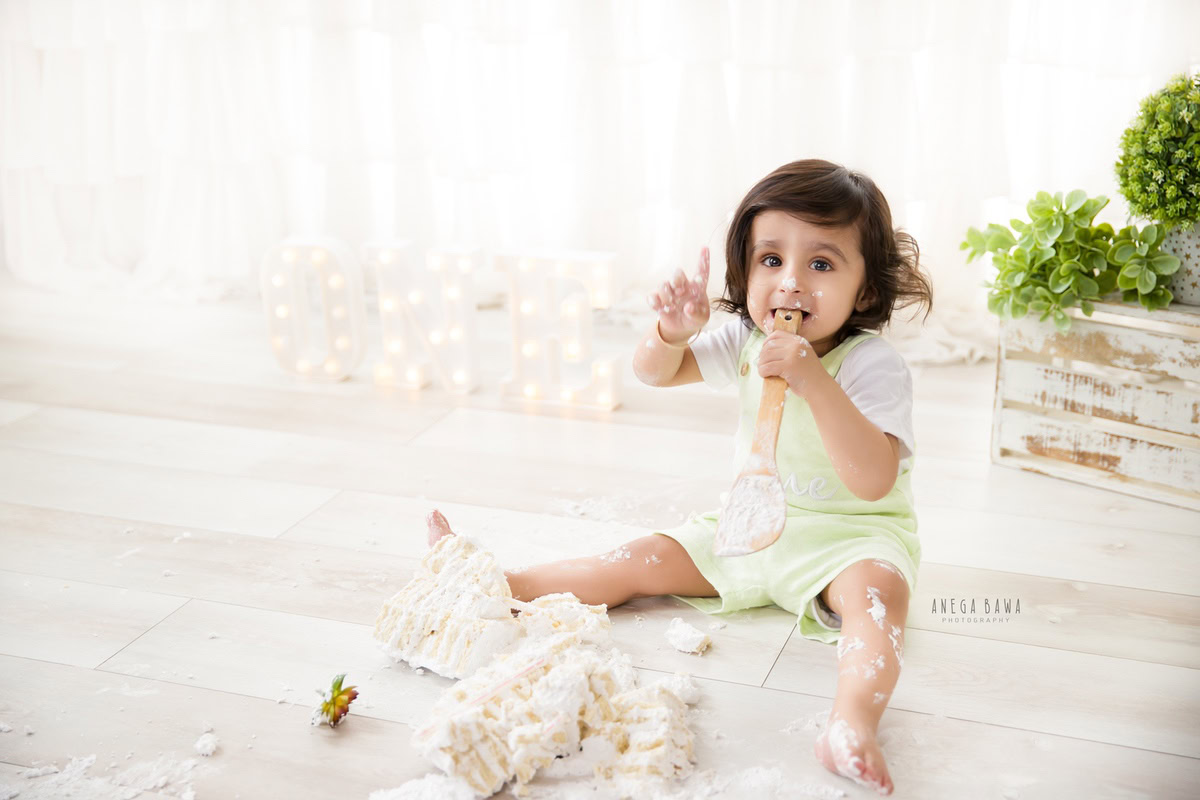 Boy with Cake Smash, white backdrop, first birthday photoshoot in Delhi, Gurgaon. Captured by Anega Bawa family photographer Gurgaon (Delhi NCR)