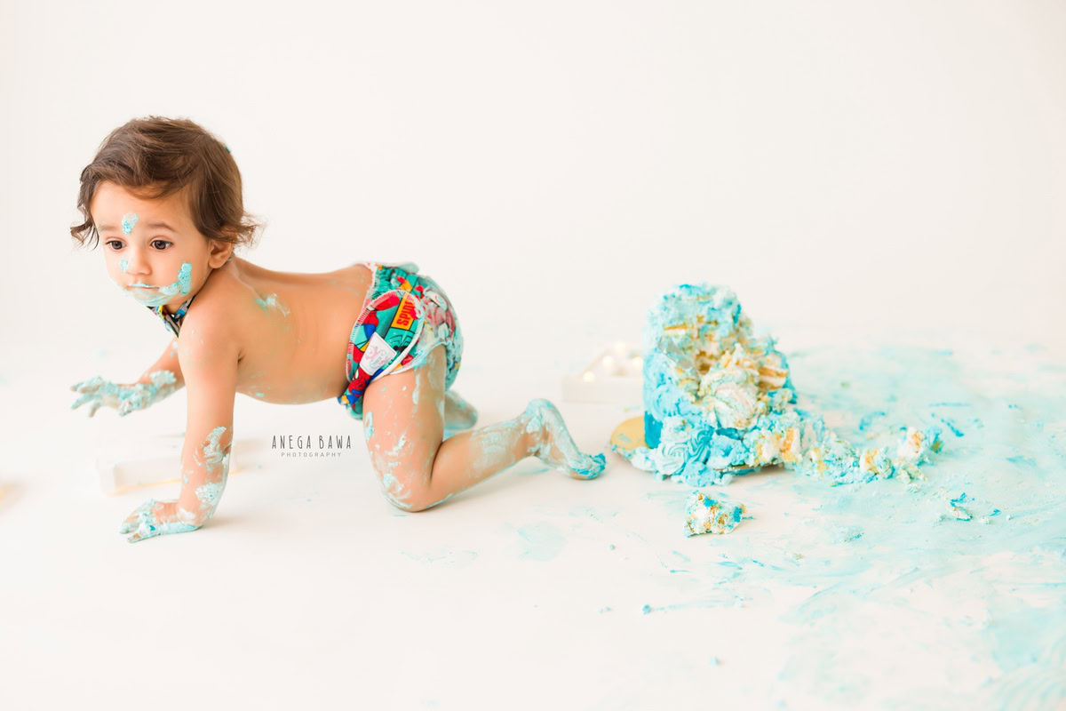 Boy crawling with cake smash on face, white backdrop, adorable first birthday photoshoot in Delhi, Gurgaon by Anega Bawa.