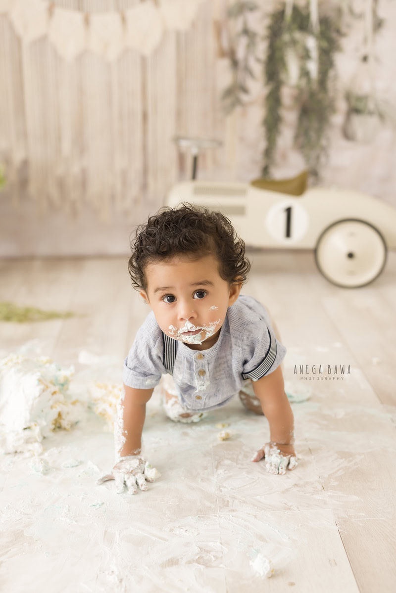 1year old boy crawling on the floor with a cake smash setup and a toy scooter against a beige backdrop, captured by Anega Bawa during a Cake Smash photoshoot in Delhi, Gurgaon