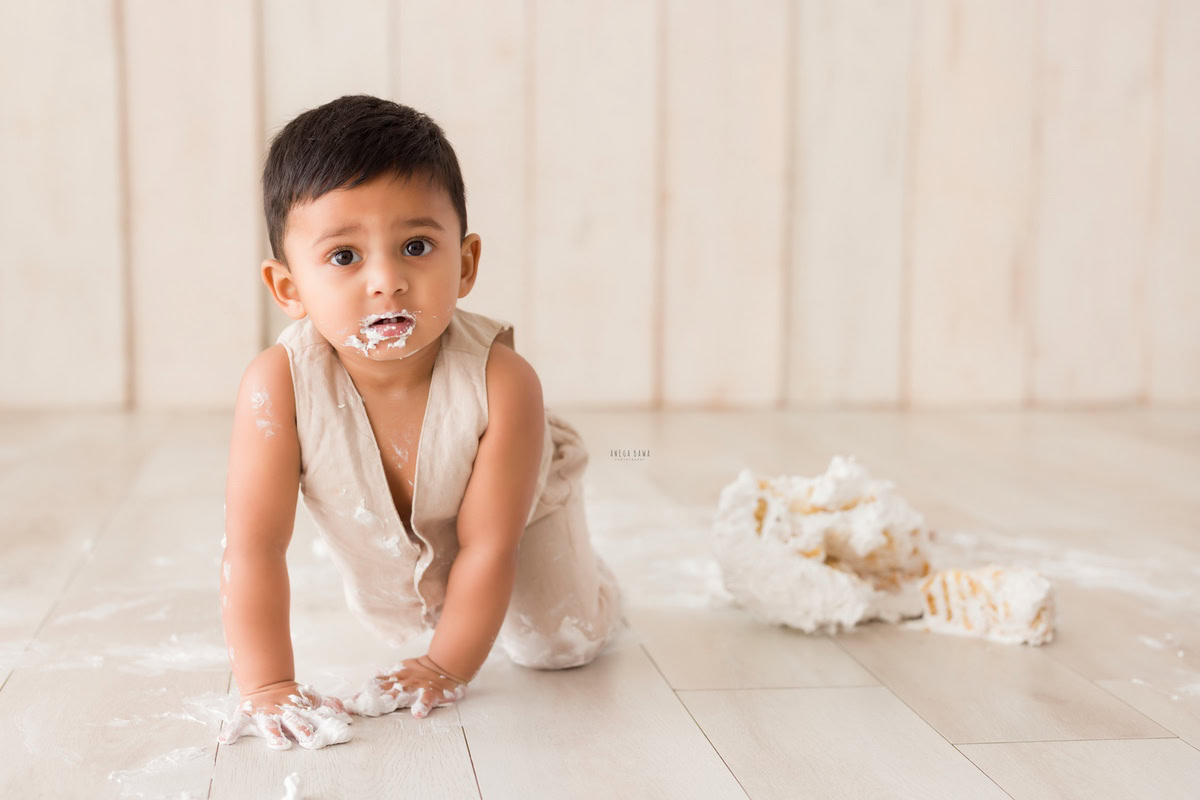 Boy crawling on the floor with Cake Smash on face, beige backdrop, first birthday photography in Delhi, Gurgaon. Captured by Anega Bawa family photographer Gurgaon (Delhi NCR)