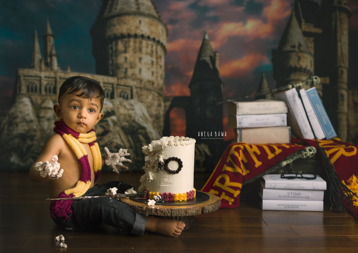 1year old boy enjoying a cake smash setup with a Harry Potter-themed backdrop and books, captured by Anega Bawa during a Cake Smash photoshoot in Delhi, Gurgaon