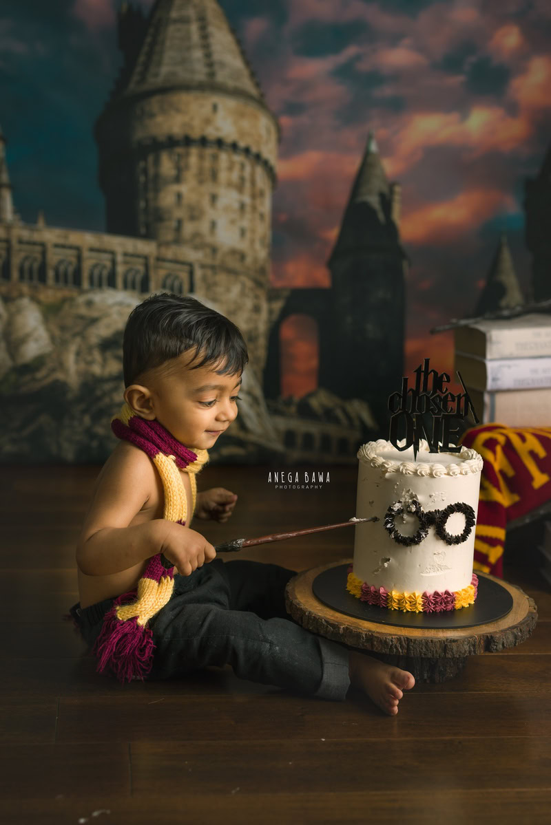 1 year boy enjoying a cake smash setup with a Harry Potter wallpaper backdrop, captured by Anega Bawa during a Cake Smash photoshoot in Delhi, Gurgaon
