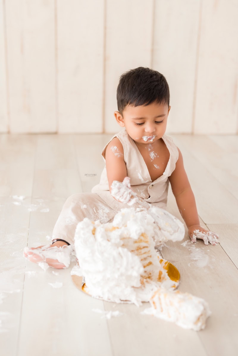 1 year boy playing with a cake smash setup against a beige backdrop, captured by Anega Bawa during a Cake Smash photoshoot in Delhi, Gurgaon