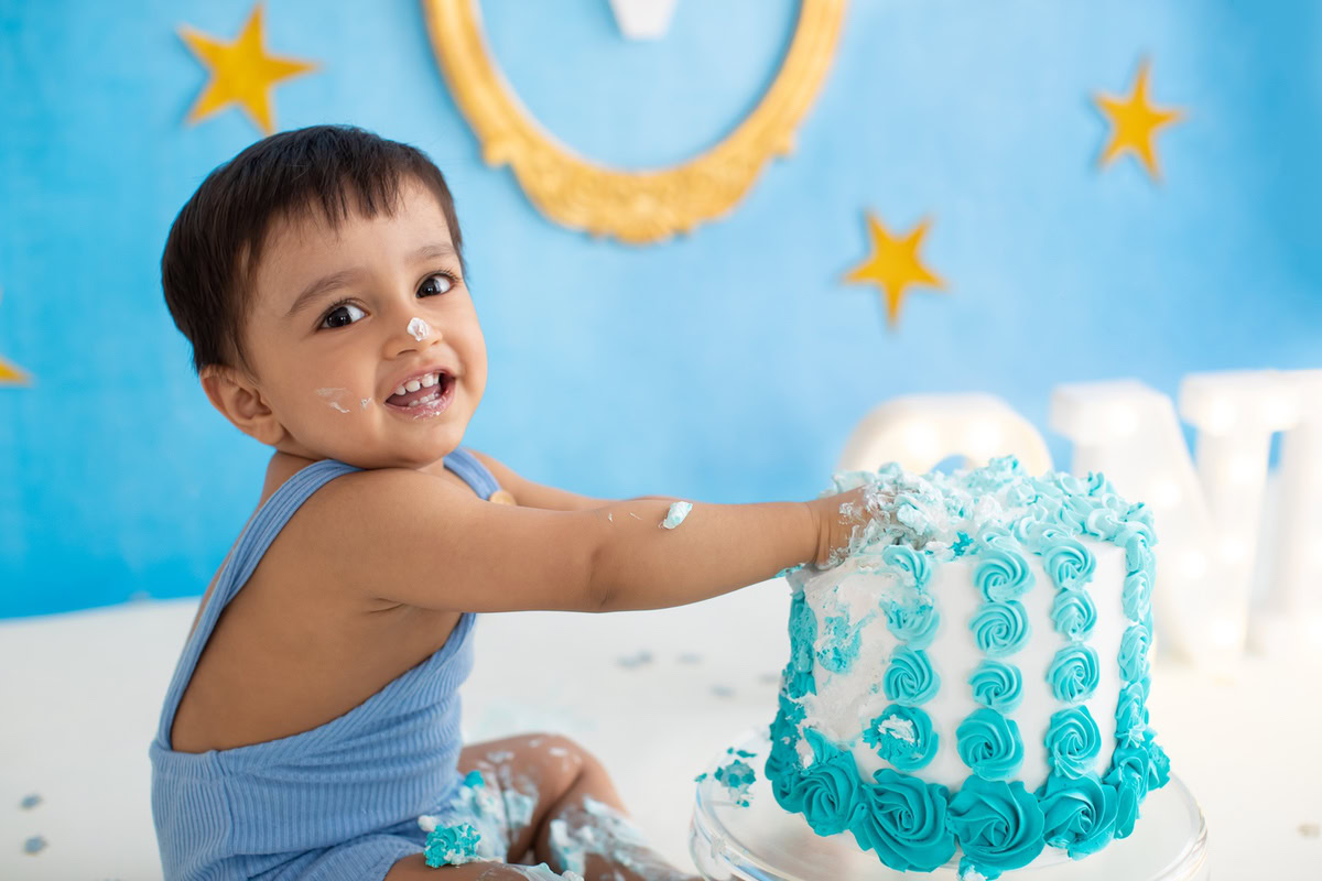Boy playing with cake smash, golden starry blue backdrop, magical first birthday photoshoot in Delhi, Gurgaon by Anega Bawa.