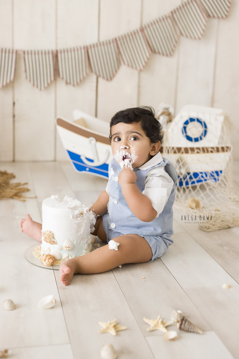 Boy playing with Cake Smash and a toy spaceship, set against a beige backdrop, first birthday photoshoot in Delhi, Gurgaon. Captured by Anega Bawa family photographer Gurgaon (Delhi NCR)