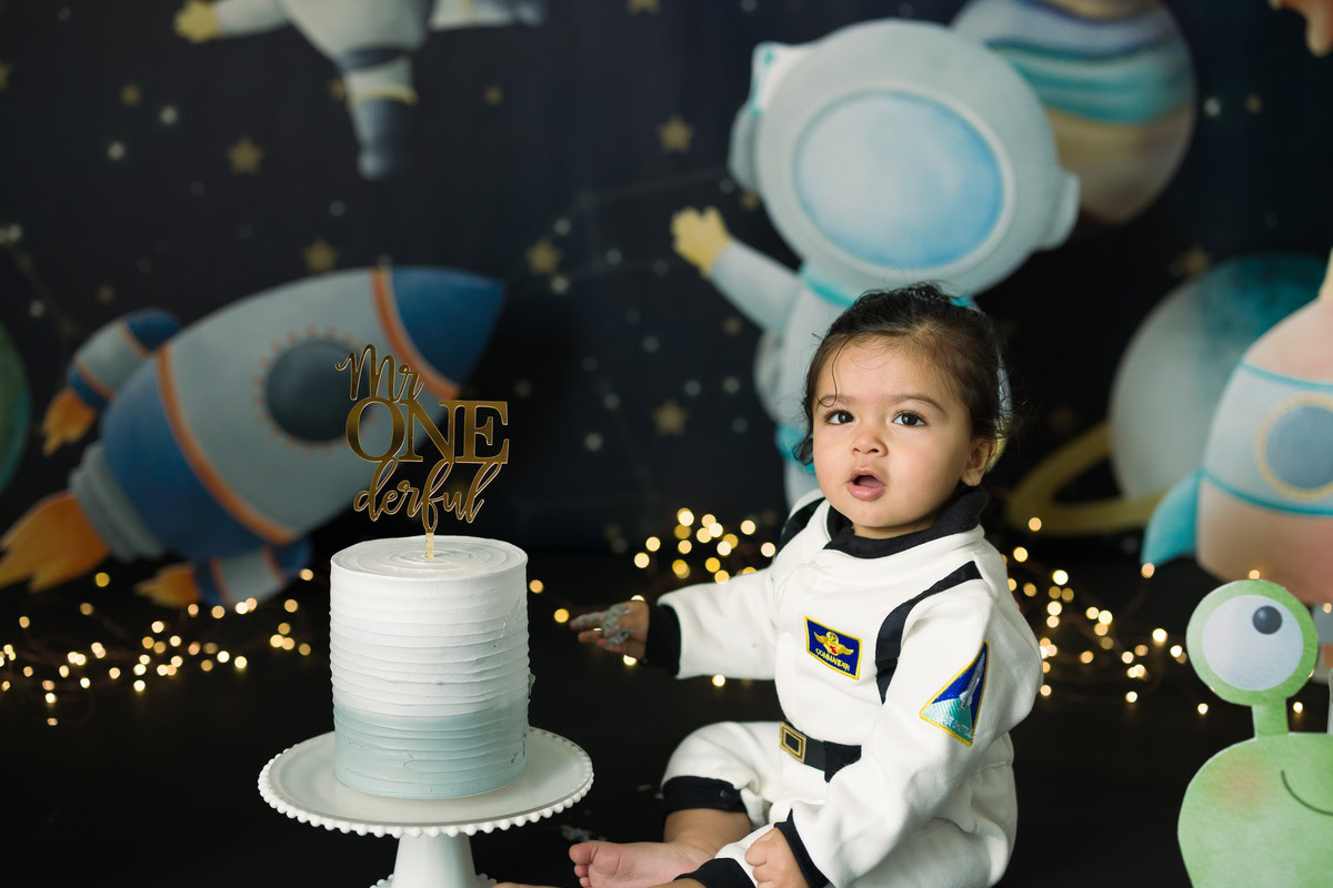 Boy posing with a cake in a spaceship backdrop with fairy lights during a Cake Smash photoshoot by well-known Anega Bawa Photography in Delhi, Gurgaon.