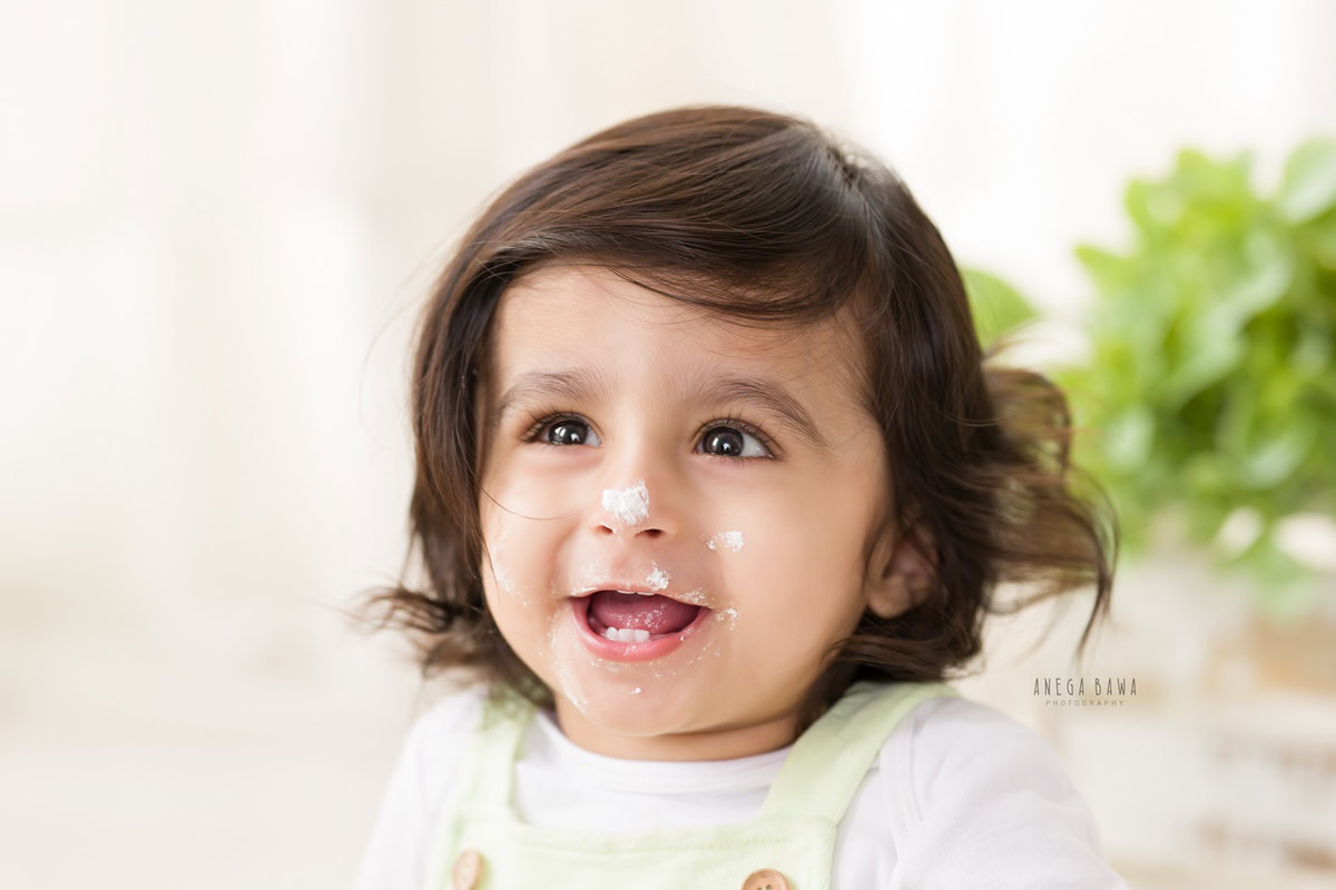 1 year old boy with cake smash on his face against a white backdrop. Captured during a delightful first birthday photoshoot in Delhi Gurgaon by the renowned family photographer Anega Bawa.