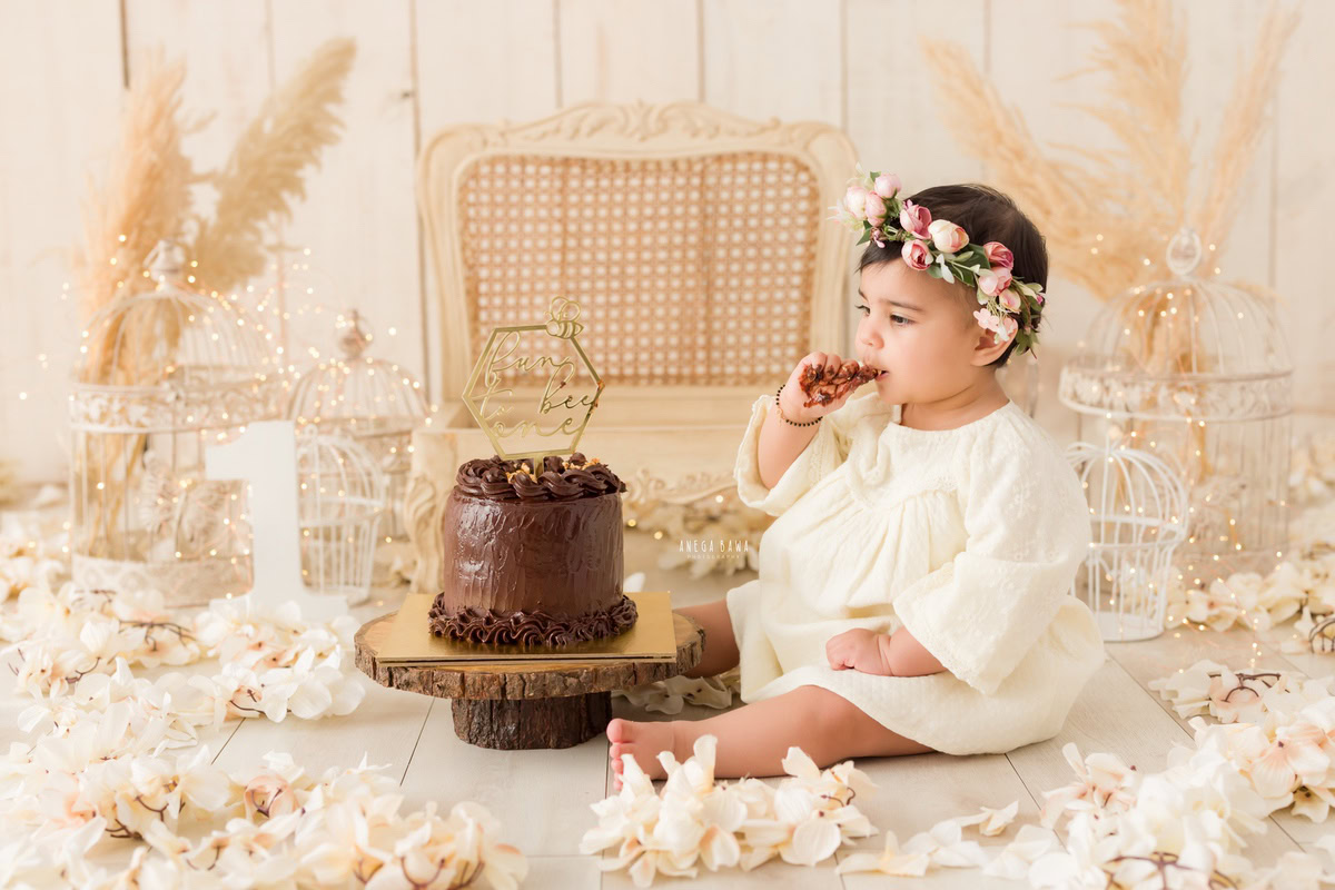 Girl enjoying a cake with white castles and a wooden chair against a beige backdrop during a Cake Smash photoshoot by well-known Anega Bawa Photography in Delhi, Gurgaon.