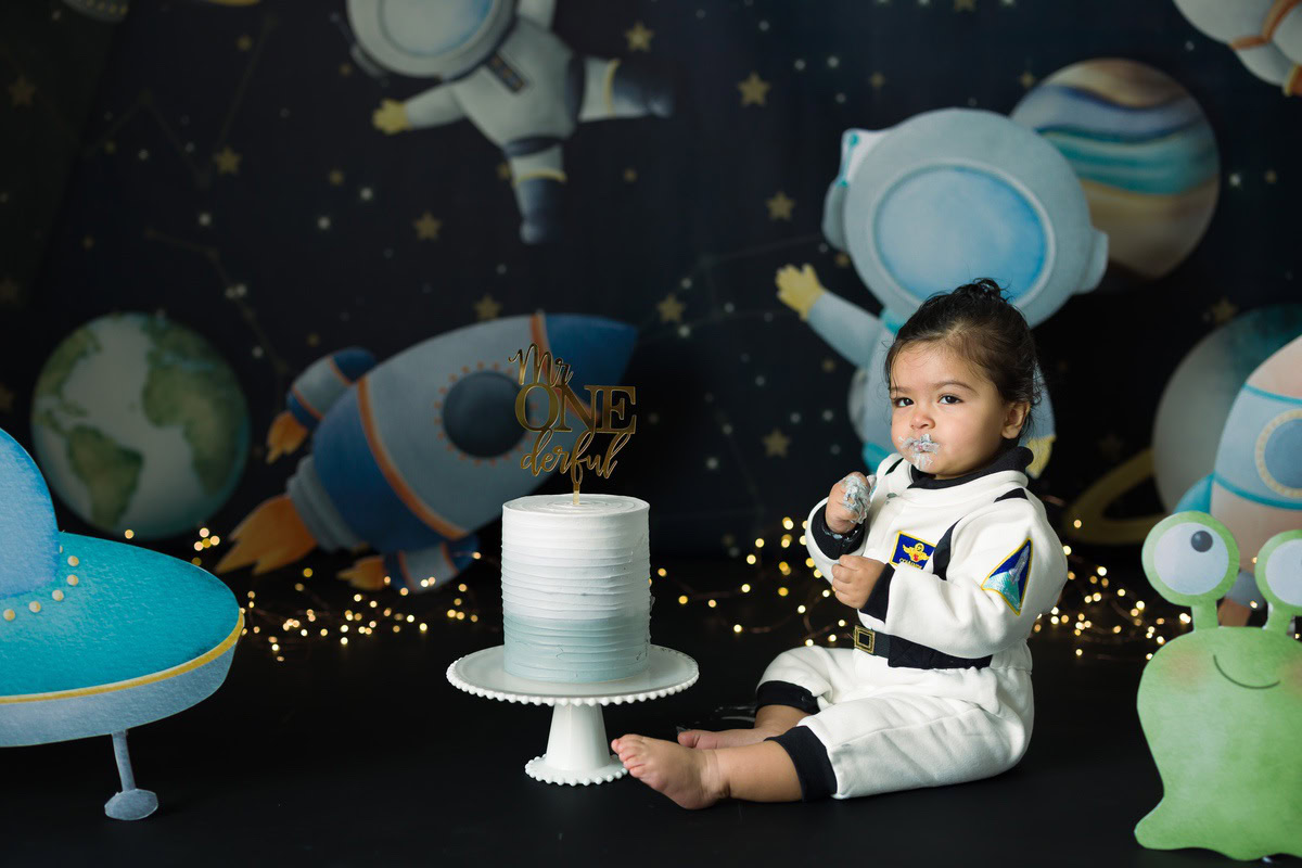 Girl posing with Cake Smash, set against a space-themed backdrop with twinkling fairy lights, captured in a magical Cake Smash photoshoot by Anega Bawa in Delhi, Gurgaon.