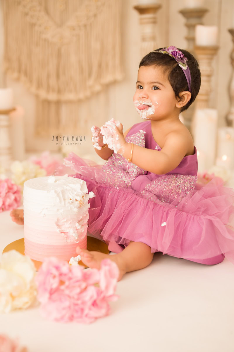 Girl sitting on the floor with Cake Smash, against a beige backdrop with a candle stand, captured in a charming Cake Smash photography session by Anega Bawa in Delhi, Gurgaon.