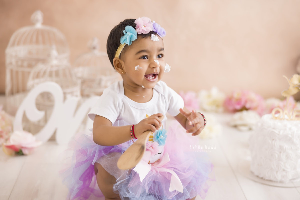 Girl sitting on the floor with Cake Smash, surrounded by castles and a peach backdrop, captured in a delightful Cake Smash photoshoot by Anega Bawa in Delhi, Gurgaon.