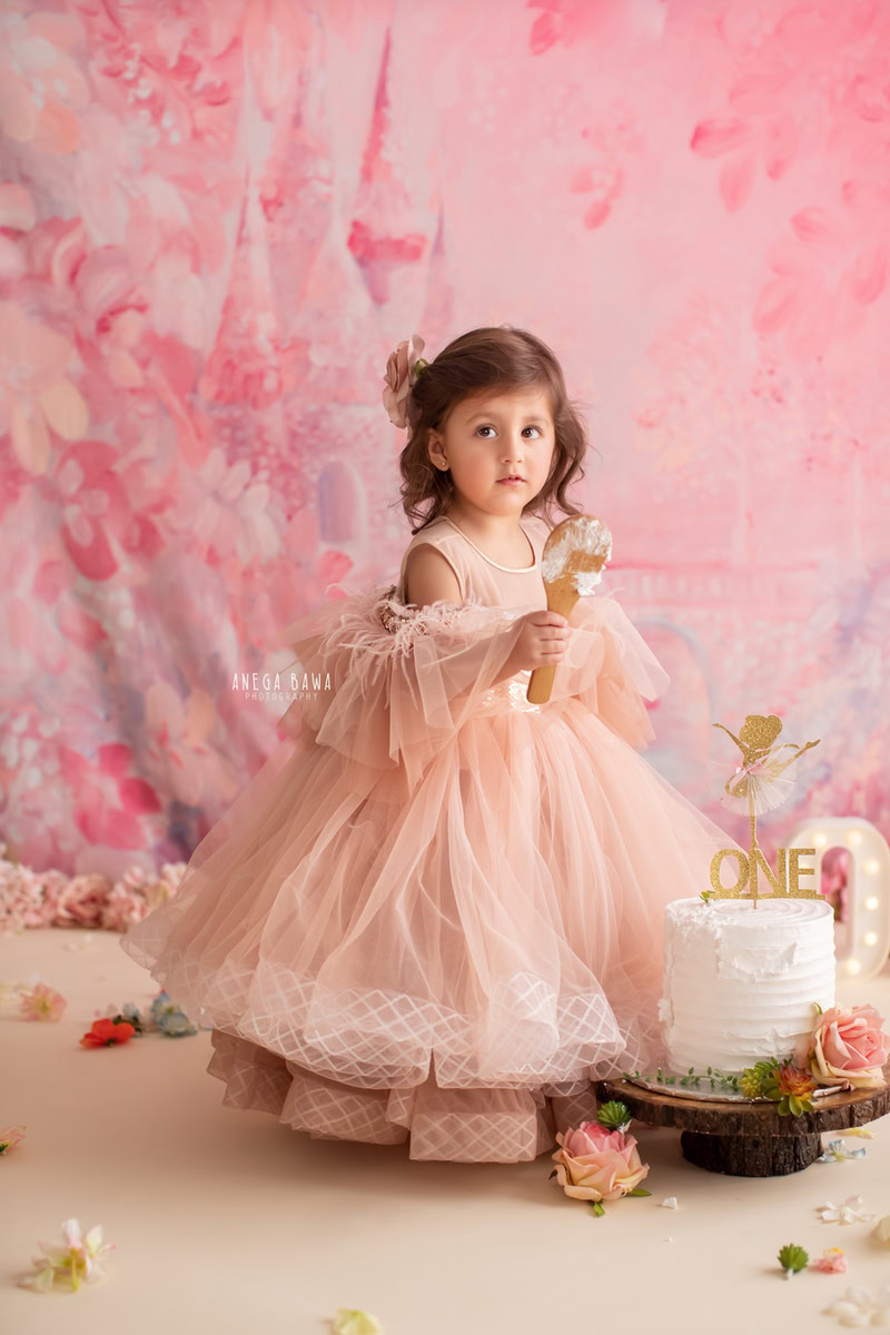 Girl standing with Cake Smash, set against a vibrant pink backdrop, captured in a stunning Cake Smash photoshoot by Anega Bawa in Delhi, Gurgaon.