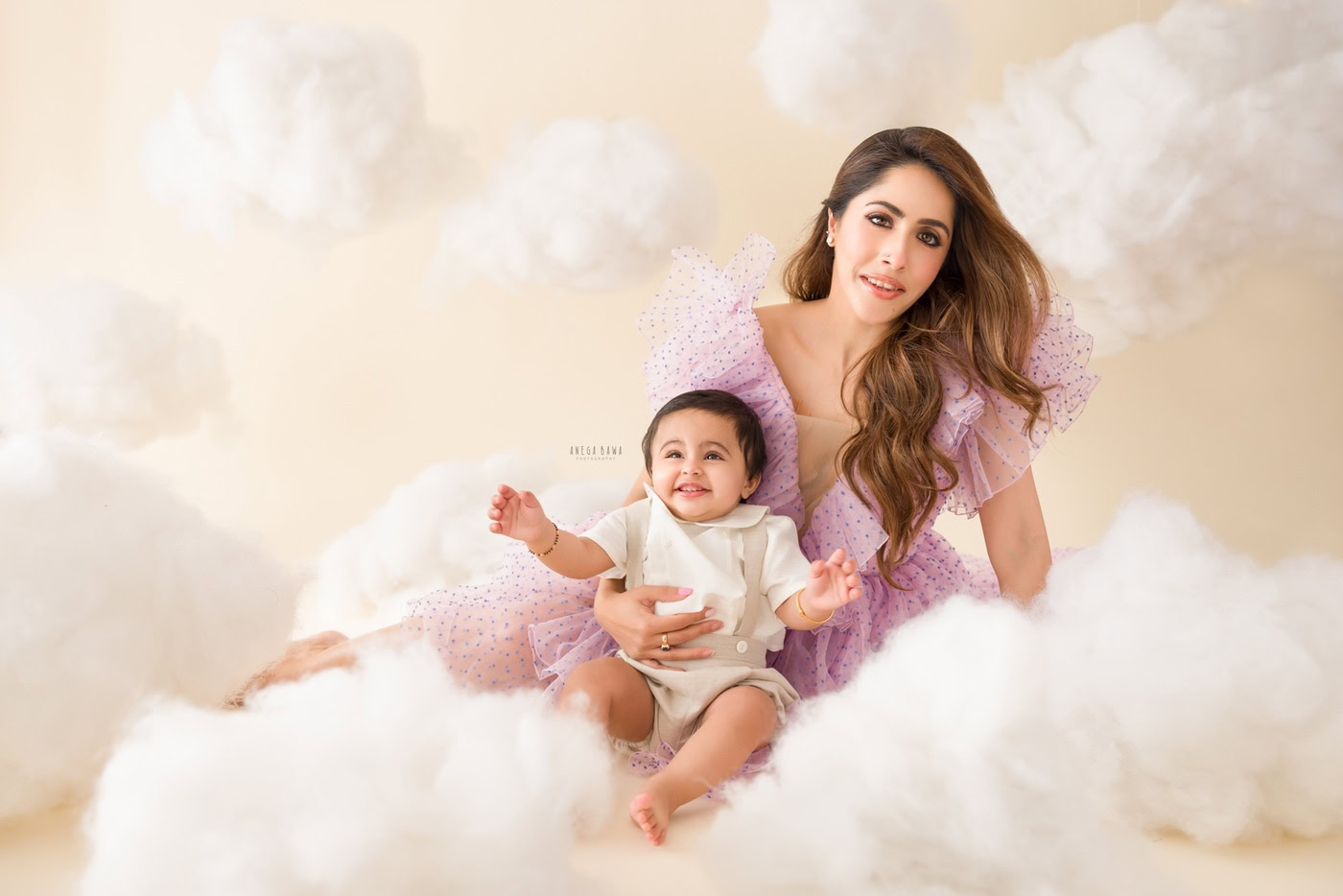 Mom and 1 year boy posing on a cotton-like snowy floor with a beige cloudy backdrop, captured during a family photography session by Anega Bawa in Delhi, Gurgaon. The setting beautifully highlights their connection and natural expressions.
