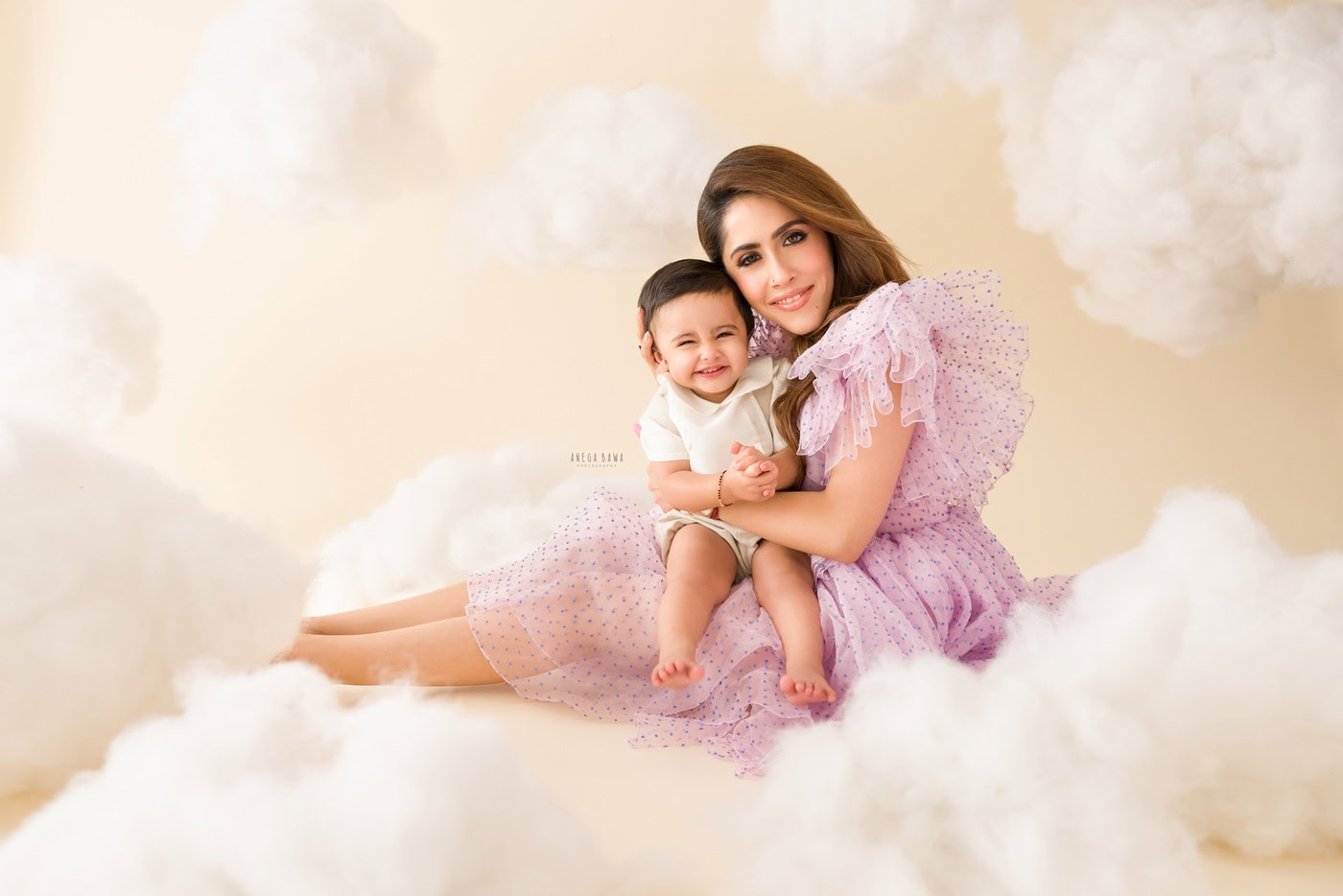 Mom and 1 year boy posing on a cotton-like snowy floor against a beige cloudy backdrop, captured during a family photography session by Anega Bawa in Delhi, Gurgaon. The serene setting enhances the bond, emphasizing the natural moments.