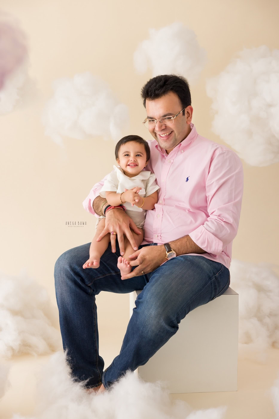 12 month boy posing with dad in a smiling pose against a beige cloudy backdrop, captured during a family photography session by Anega Bawa in Delhi, Gurgaon. The soft background enhances their joyful expressions and the warmth of the moment.
