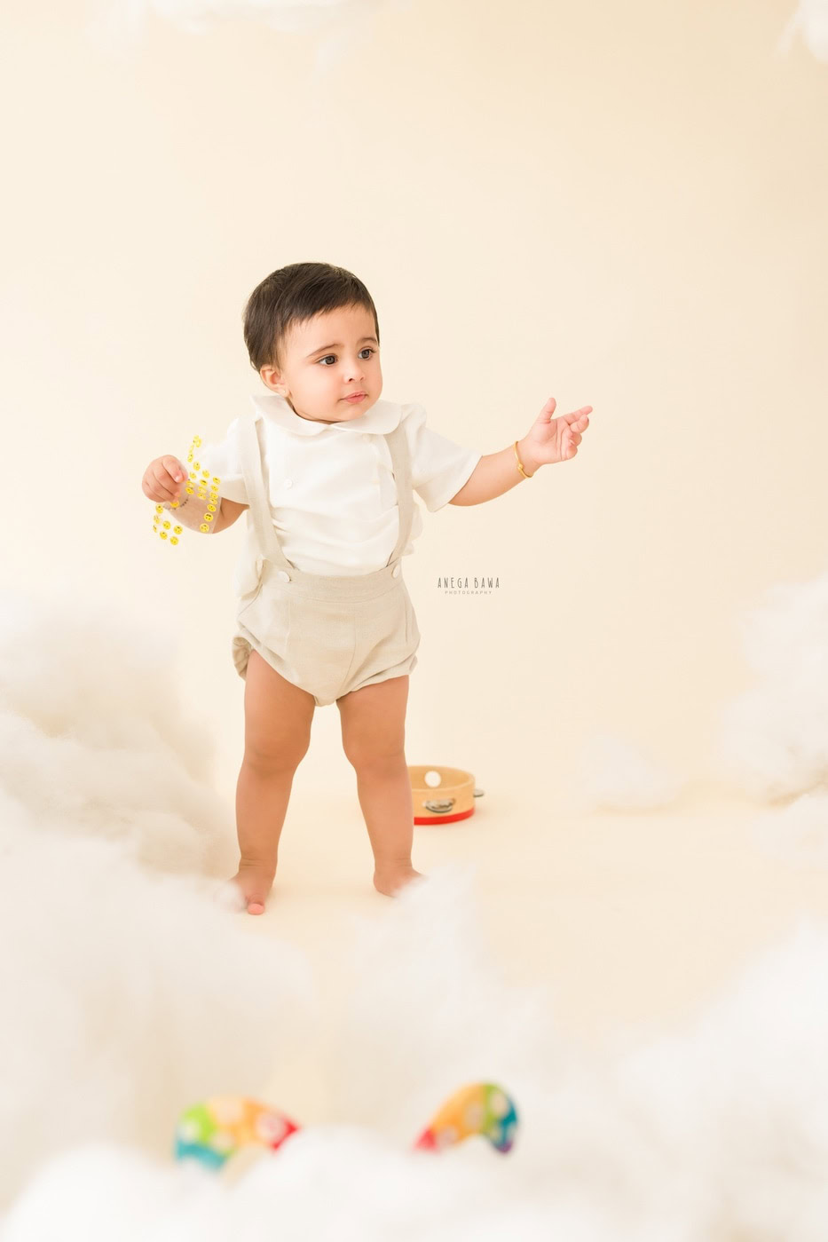 15 month boy standing on a snowy rug against a white backdrop, captured during a family photography session by Anega Bawa in Delhi, Gurgaon. His playful stance adds a charming touch to the serene setting.