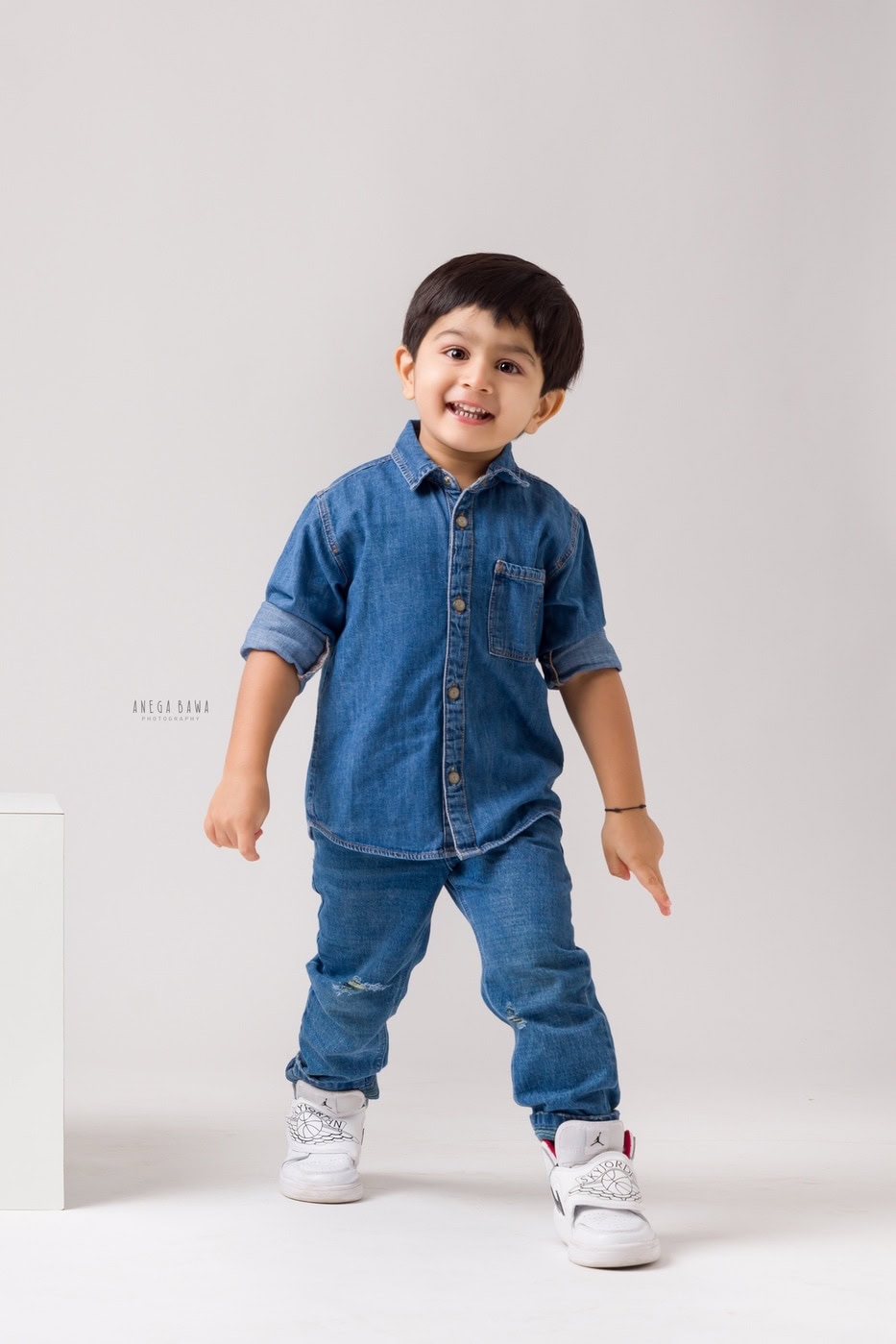2 year boy posing in an all-denim look against a white backdrop, captured during a family photography session by Anega Bawa in Delhi, Gurgaon. The clean background emphasizes his playful personality and style.