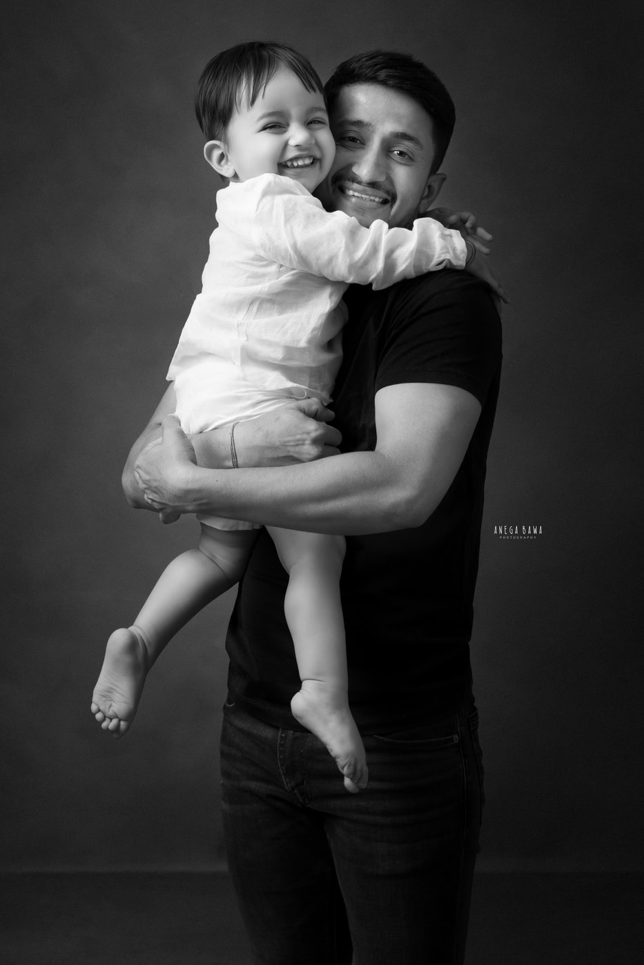 2 year boy posing cutely with his uncle against a black backdrop in a black-and-white family photography session by Anega Bawa in Delhi, Gurgaon. The classic tones highlight their playful connection and expressions.