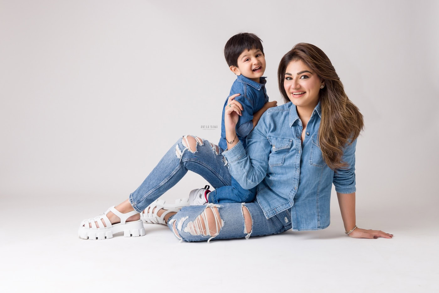 3 year boy posing with mom lying on the floor, both wearing denim shirts against a white backdrop, captured during a family photography session by Anega Bawa in Delhi, Gurgaon. Their twinning outfits and playful poses create a charming family moment.