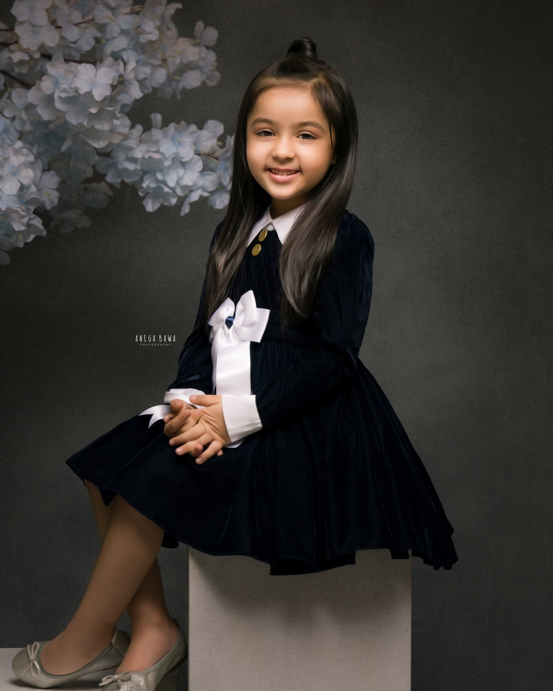 3 year girl posing cutely in a black-and-white dress against a black backdrop, captured during a family photography session by Anega Bawa in Delhi, Gurgaon. Her smiling pose adds a delightful touch to the elegant setting.