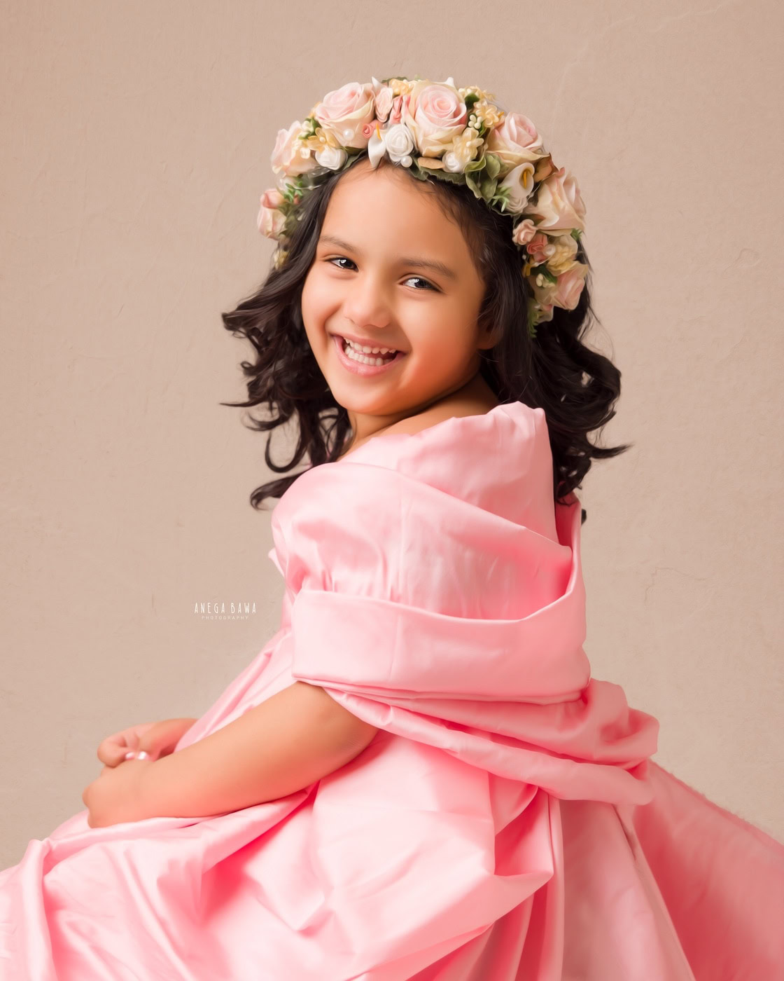 3-year-old girl wearing a pink wrap dress and a tiara band, in a cute smiling pose during a family photography session by Anega Bawa in Delhi, Gurgaon. Her joyful expression and charming outfit beautifully capture her playful personality.