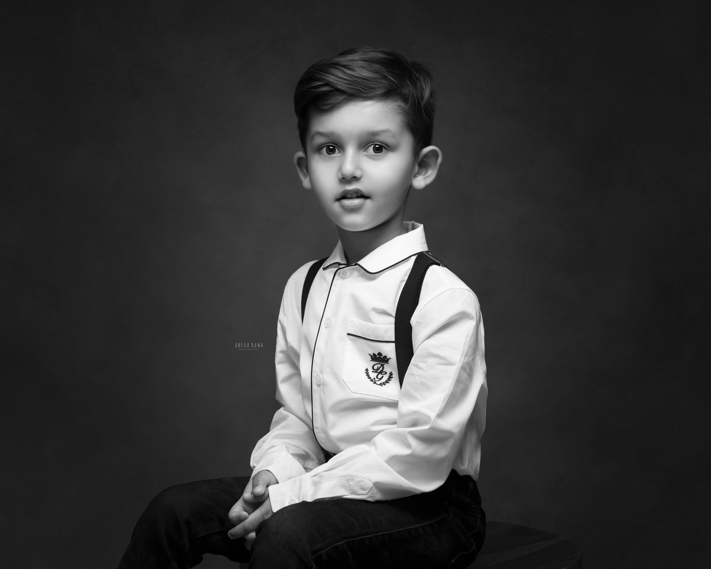 3 year boy posing smartly in a white shirt against a black backdrop in a black-and-white family photography session by Anega Bawa in Delhi, Gurgaon. The classic contrast highlights his charming personality and style.