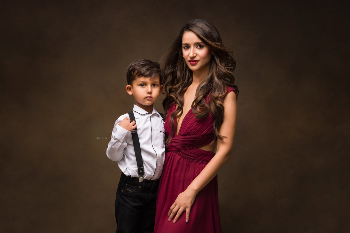 3 year boy wearing a white shirt, posing cutely with mom against a brown backdrop, captured during a family photography session by Anega Bawa in Delhi, Gurgaon. Their warm expressions highlight the special bond between them.