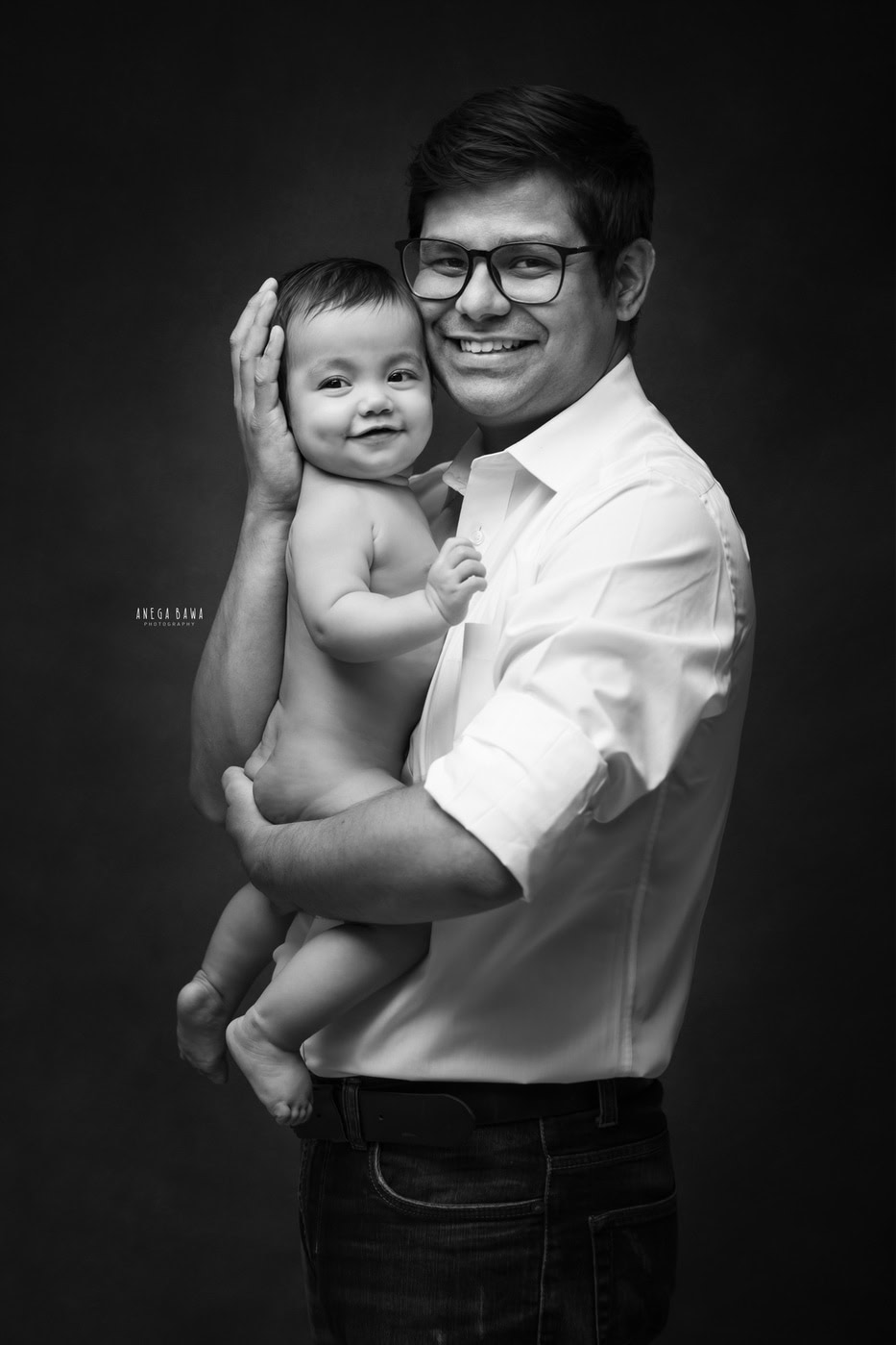 Dad holding his son in his arms against a black backdrop, captured during a family photography session by Anega Bawa in Delhi, Gurgaon. The simple setting highlights their loving bond and the joy of the moment.