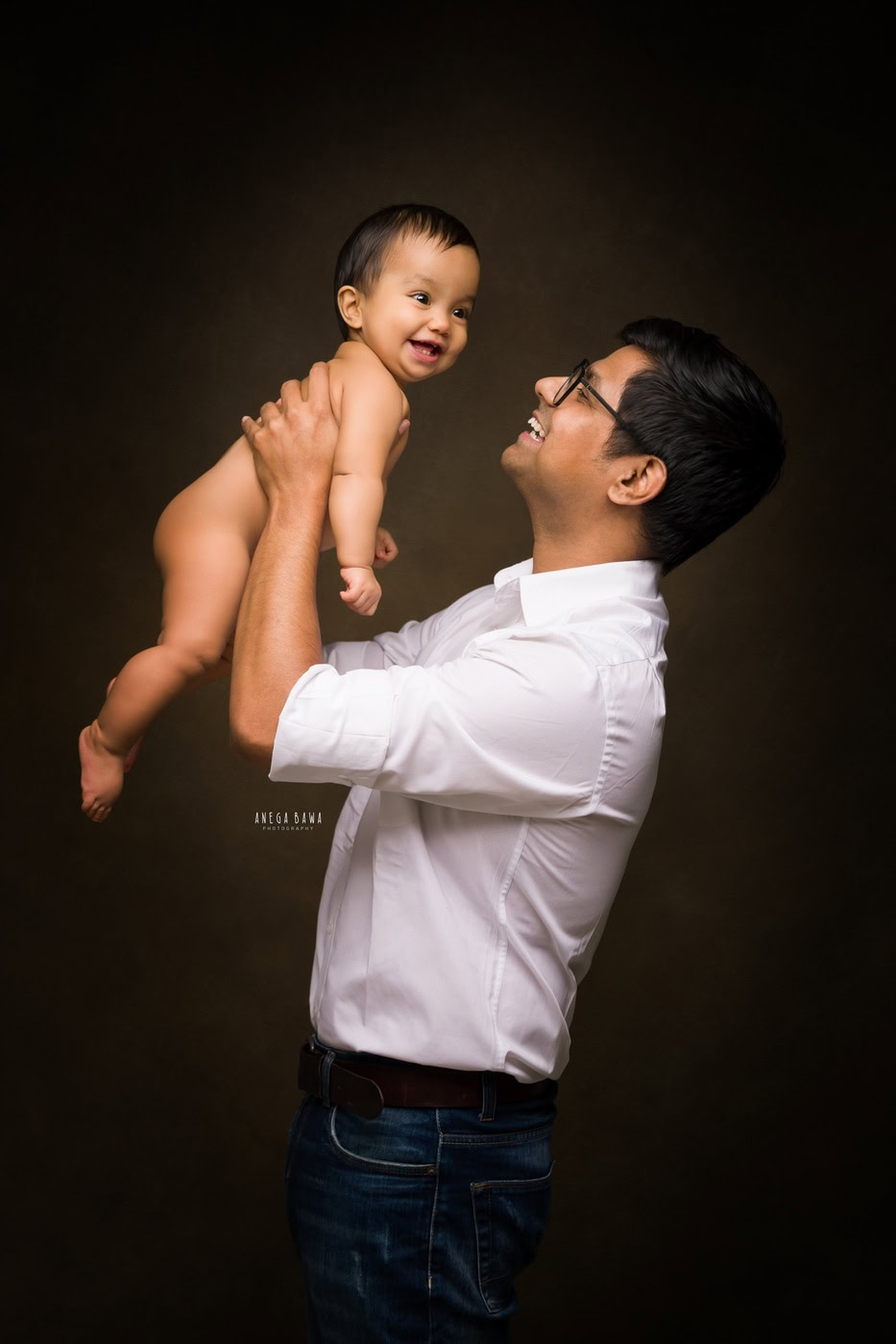 Dad posing with his son, holding him in his arms against a black backdrop, captured during a family photography session by Anega Bawa in Delhi, Gurgaon. This intimate moment beautifully showcases their close bond.
