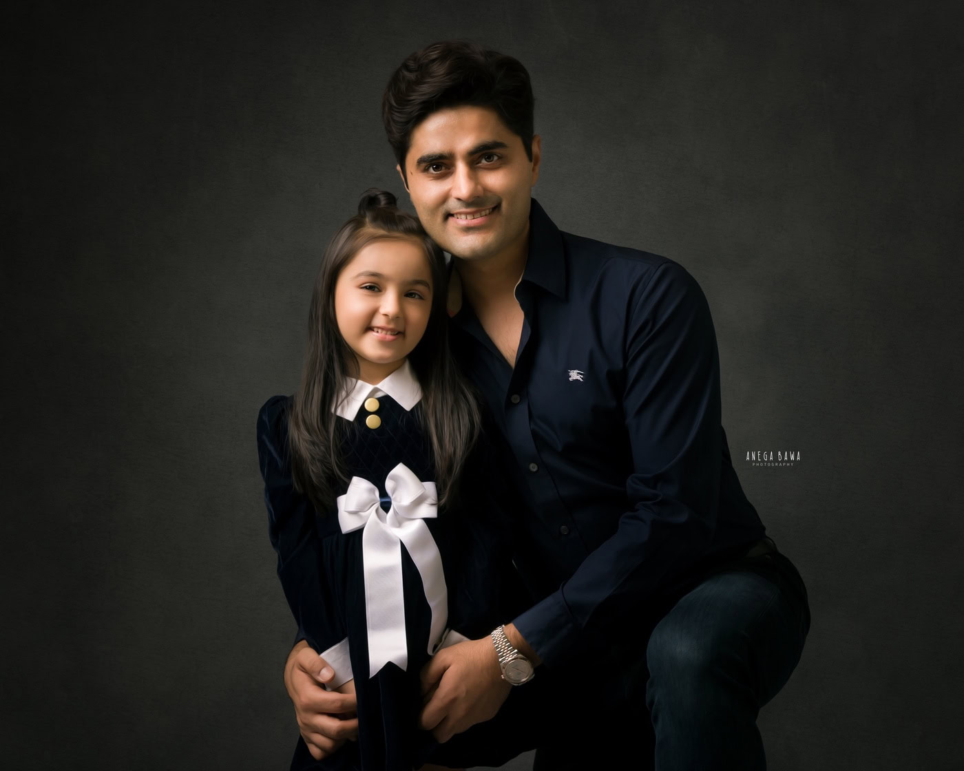 Dad posing with his cute daughter in a black-and-white dress against a grey backdrop, captured during a family photography session by Anega Bawa in Delhi, Gurgaon. Their joyful expressions highlight the special connection they share.
